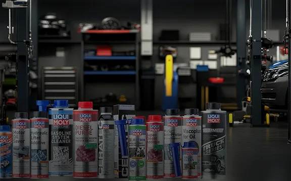 A variety of Liqui Moly automotive additives and cleaners standing in a blurred professional garage workshop.